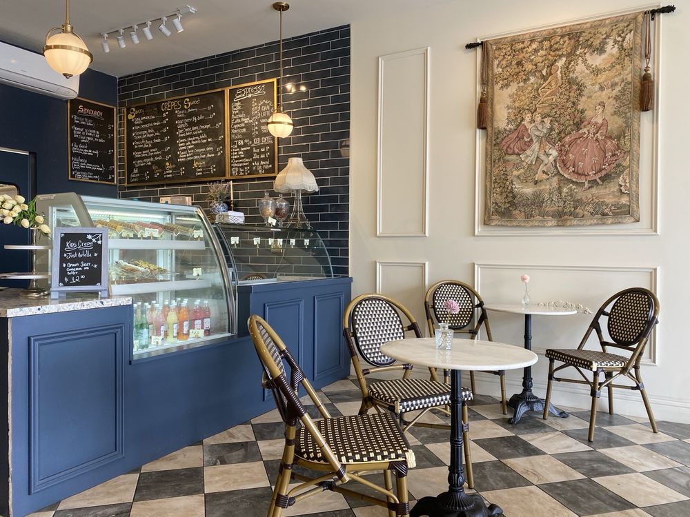 Chalkboard crêpe, sandwich and espresso menus above the navy counter, with a French tapestry on the ivory molded wall