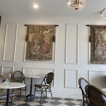 French tapestries on the ivory molded wall above marble bistro tables and woven chairs at Creperie Antoinette