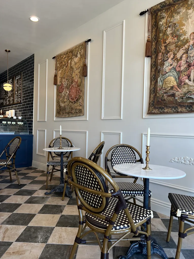 Marble tables and woven bistro chairs under two French tapestries, with the navy counter and chalkboard menus behind