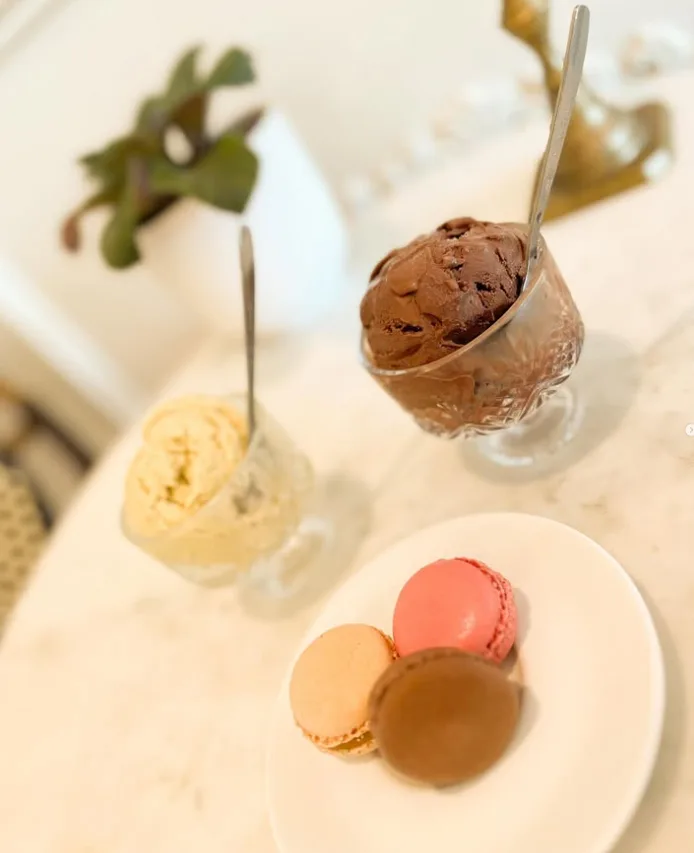 Chocolate and vanilla gelato in glass dessert cups with a plate of macarons on a marble table