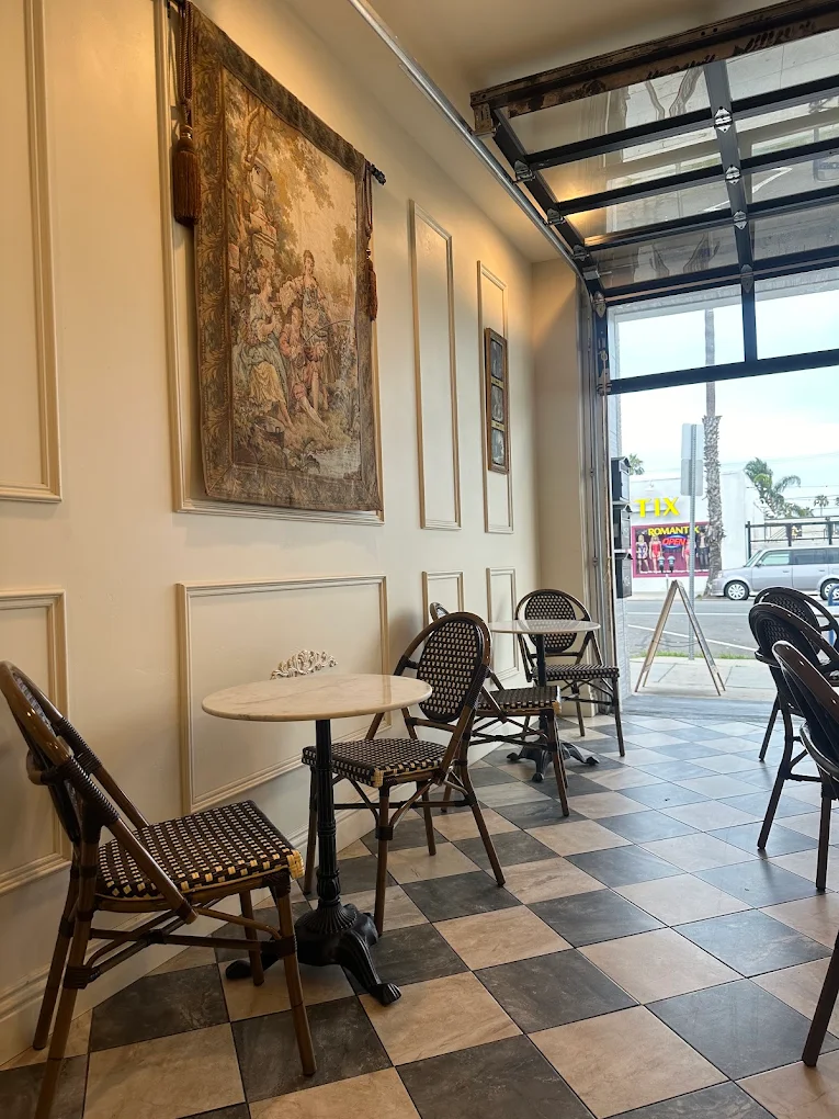 Bistro tables along the tapestry wall beside the open roll-up glass door looking onto Garnet Avenue and the palms
