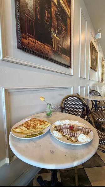 A savory crêpe and a sweet banana Nutella crêpe with whipped cream on a marble bistro table beneath a framed Paris print